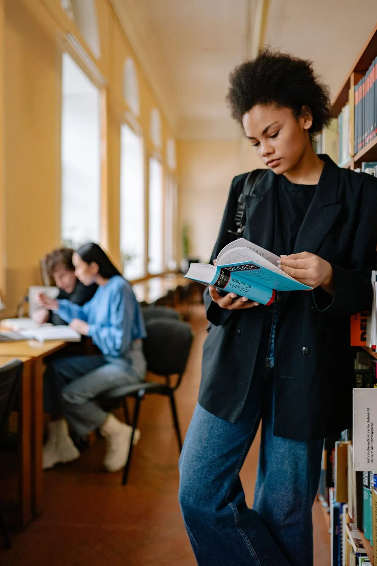 Een vrouw leunt tegen een boekenkast en leest geconcentreerd